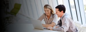 Two professionals collaborating at a laptop in a bright office, reviewing information together as part of a cloud migration strategy discussion.