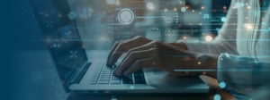 Hands typing on a laptop with transparent digital interface icons and data overlays, representing modern digital workplace technology and data-driven work.