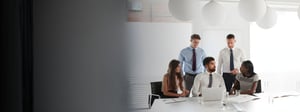Team of professionals collaborating around a laptop during a meeting in a modern office, representing IT support, help desk, or service desk teamwork.