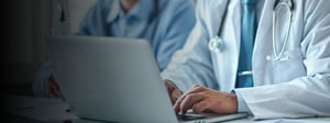Healthcare professionals using a laptop in a clinical setting, reviewing information digitally during a collaborative discussion.