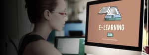 Person wearing glasses looks at a desktop monitor displaying an e-learning interface, representing online education and remote learning technology.