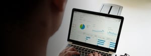 Person viewing a laptop screen displaying an analytics dashboard with charts and performance metrics, representing data analysis and legacy database reporting.