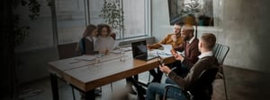 Team of professionals gathered around a conference table in a modern office, reviewing documents and discussing ideas during a collaborative meeting.