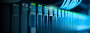 Row of server hardware with glowing indicator lights in a data center, highlighting enterprise data management and network infrastructure.