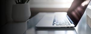 A laptop viewed from the side on a clean desk near a window, with soft natural light and minimal workspace elements, representing modern cybersecurity or endpoint protection topics.