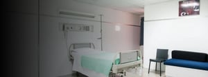 A clean, empty hospital patient room with a single bed, IV stand, and seating area, representing outsourced hospital services and healthcare operations.