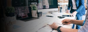 Team collaborating around a desk with laptops, monitors, and printed diagrams, representing managed services planning, IT strategy development, and coordinated operational support in a modern workplace.