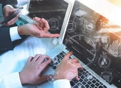Hands using a laptop and tablet with overlaid digital interface icons, representing integrated IT services, data analysis, and business technology management.